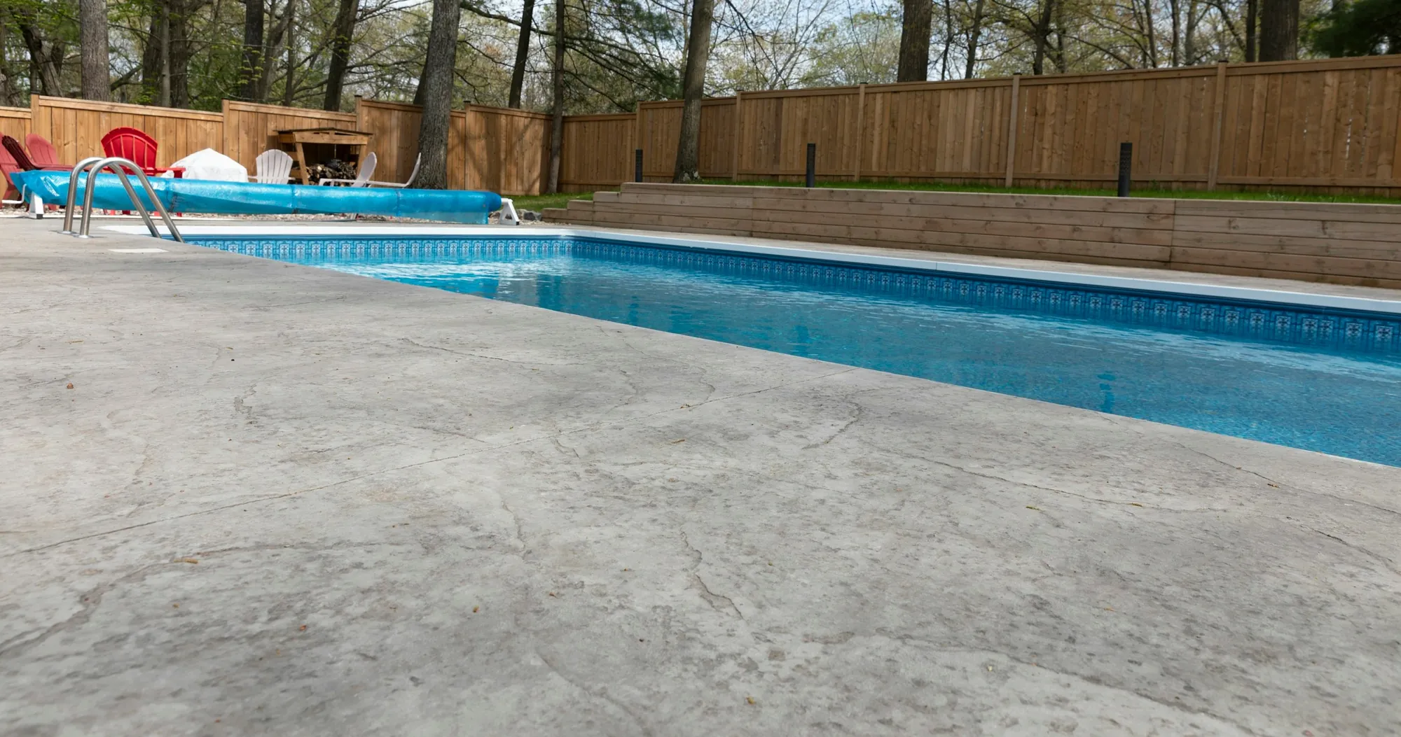 Broom-finish concrete patio around a backyard pool with a wood fence