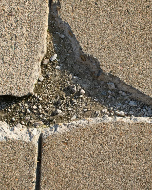 Broken sidewalk slab with a wide crack and crumbling edge