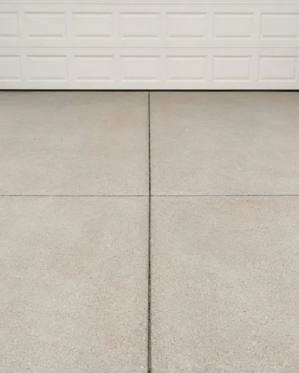 Light grey broom-finish concrete driveway in front of a white garage door