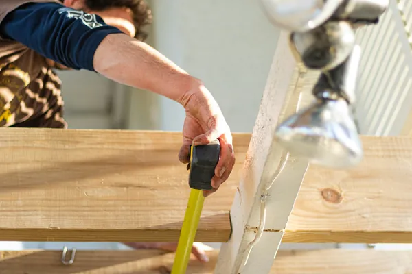 Hands holding a tape measure against a piece of framing lumber