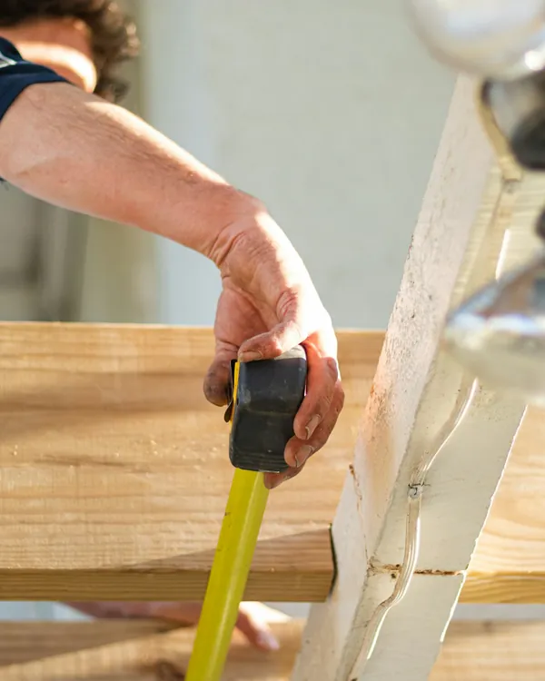 Hands measuring a length of lumber with a tape