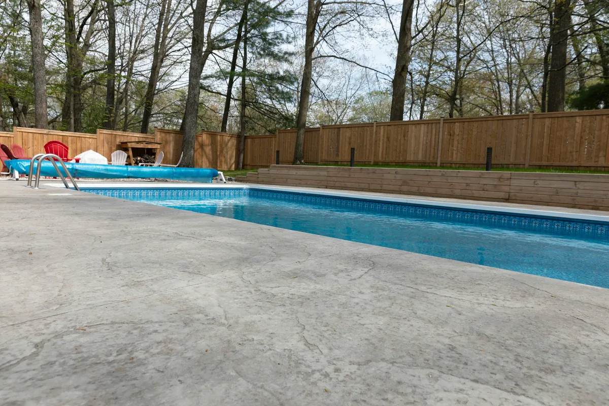Broom-finish concrete patio around a backyard pool with a wood fence