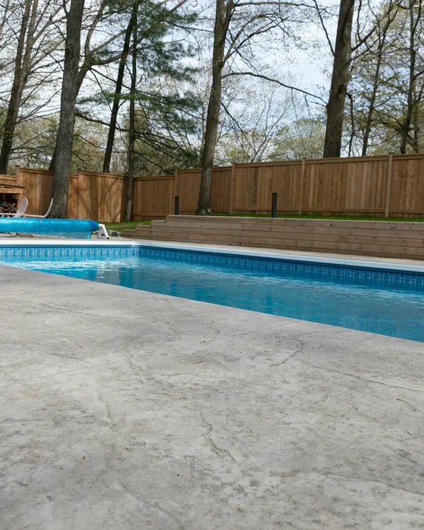 Broom-finish concrete patio around a backyard pool with a wood fence