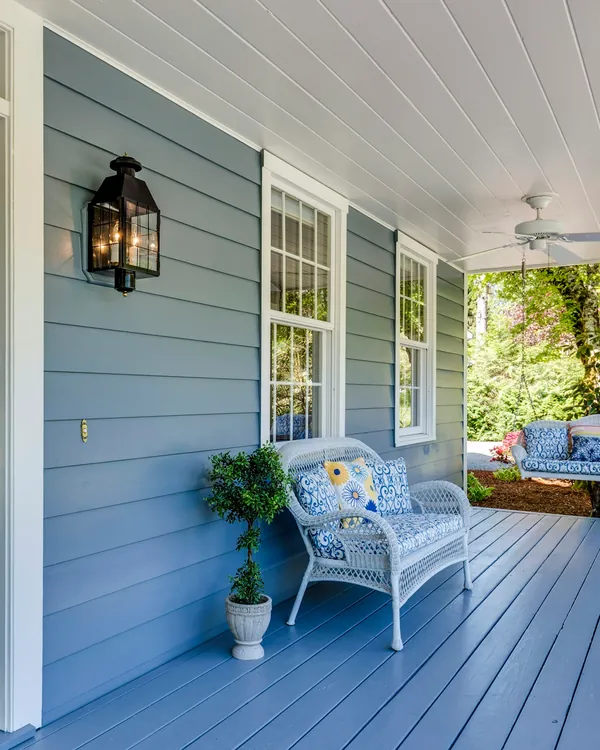 Blue covered porch with a black front door, white wicker bench and lantern