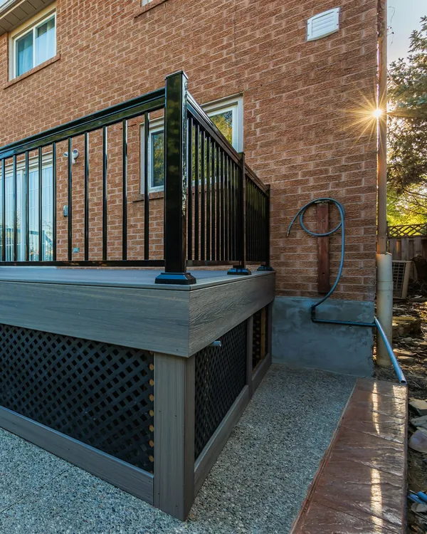 Composite deck with black aluminum railing and stairs beside a brick house