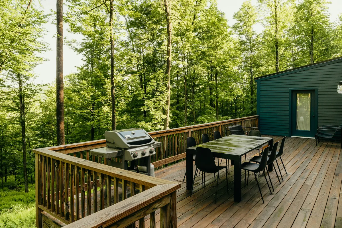 Wood deck with dining table and grill under tall trees